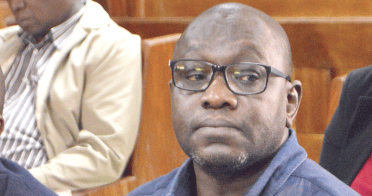 Dr Ekuru Aukot seated on a wooden bench in a Kenyan courtroom, wearing glasses and a blue shirt